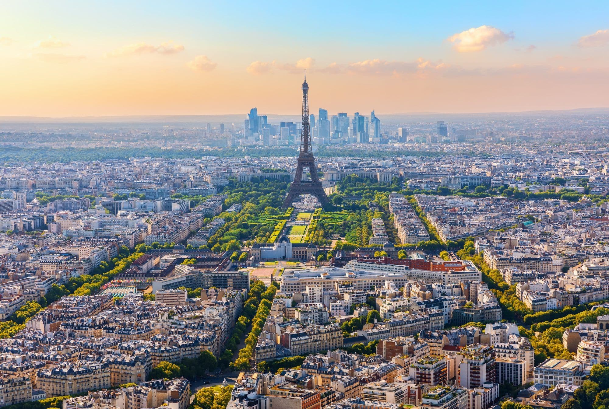 Vue aérienne de Paris au coucher du soleil, la tour Eiffel et le Champ-de-Mars au premier plan, la Défense à l'horizon